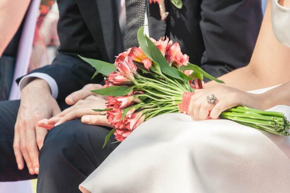 Detalle de las manos de los novios y el ramo durante la boda